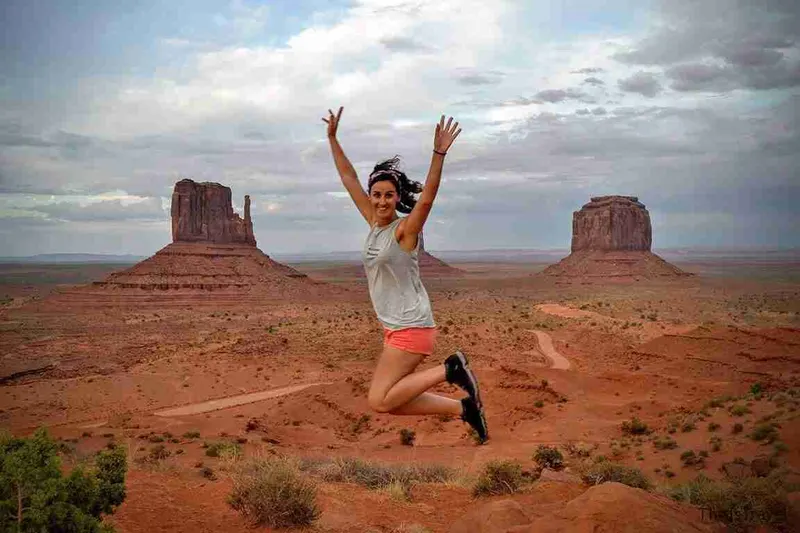 Viajera saltando ante los Mittens de Monument Valley