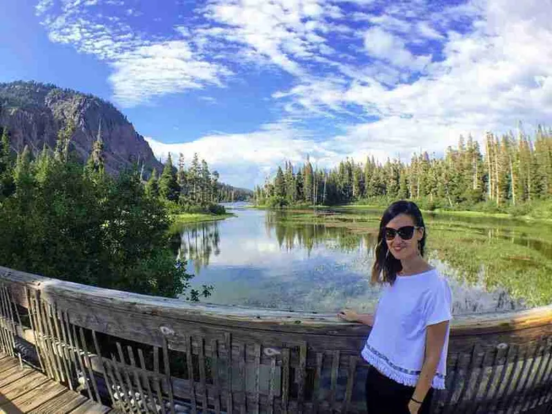 Viajera con gafas de sol en un mirador sobre un lago entre pinares