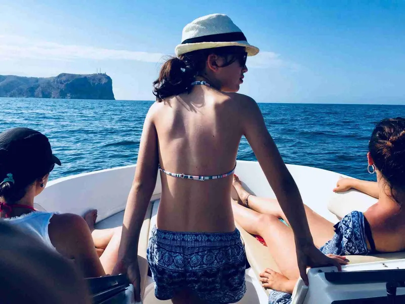 Mujer con sombrero en la proa de la lancha, mirando el mar
