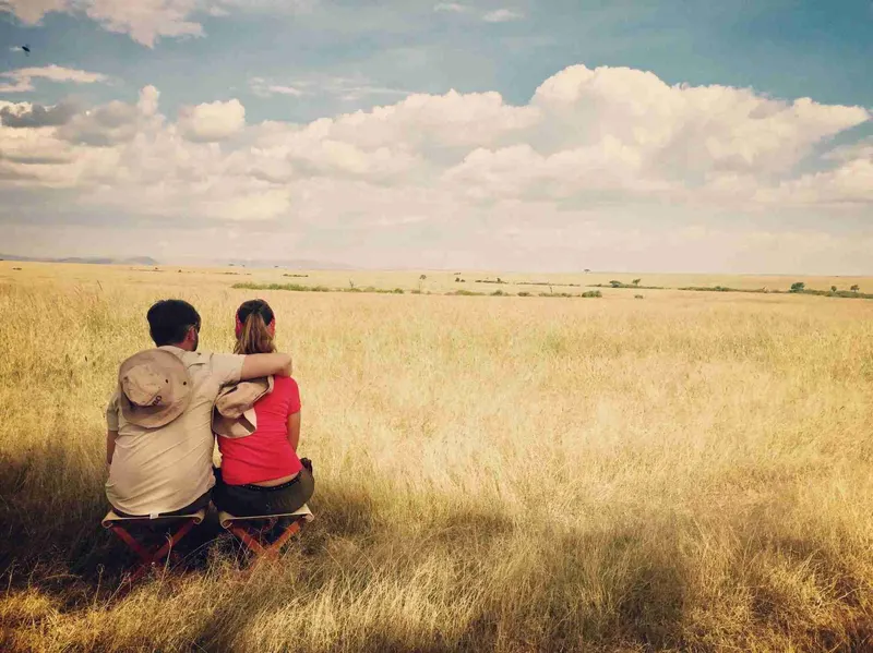 Pareja sentada en la hierba de la sabana mirando al horizonte en Masai Mara