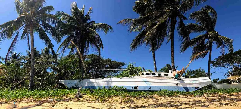 Barca de madera varada entre palmeras en una playa de Corón