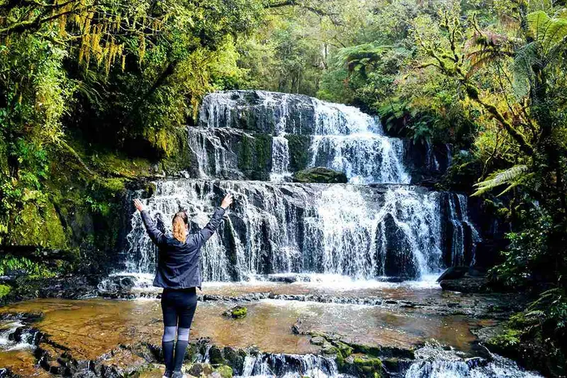 Persona bajo la cortina de agua de una cascada de Nueva Zelanda