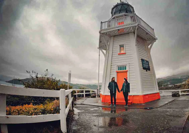 Faro blanco de Akaroa con una pareja delante, en un día gris