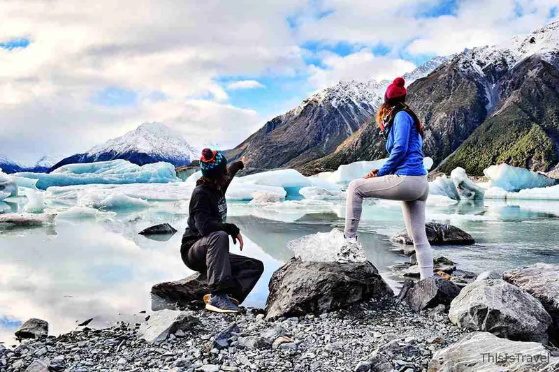 Dos personas sobre las rocas ante un glaciar de Nueva Zelanda