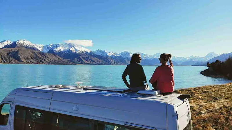 Dos personas sentadas en el techo de la campervan mirando un lago de Nueva Zelanda