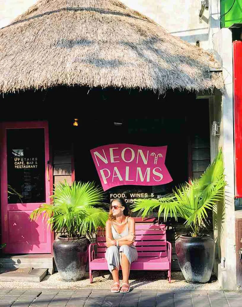 Mujer sentada ante el rótulo rosa de Neon Palms, en Seminyak