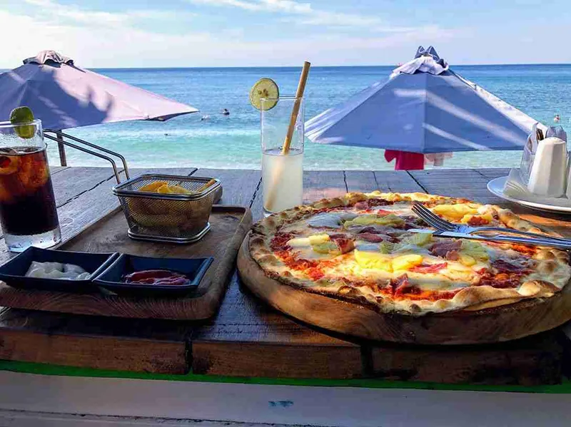 Pizza y cócteles en una mesa a pie de playa, bajo una sombrilla