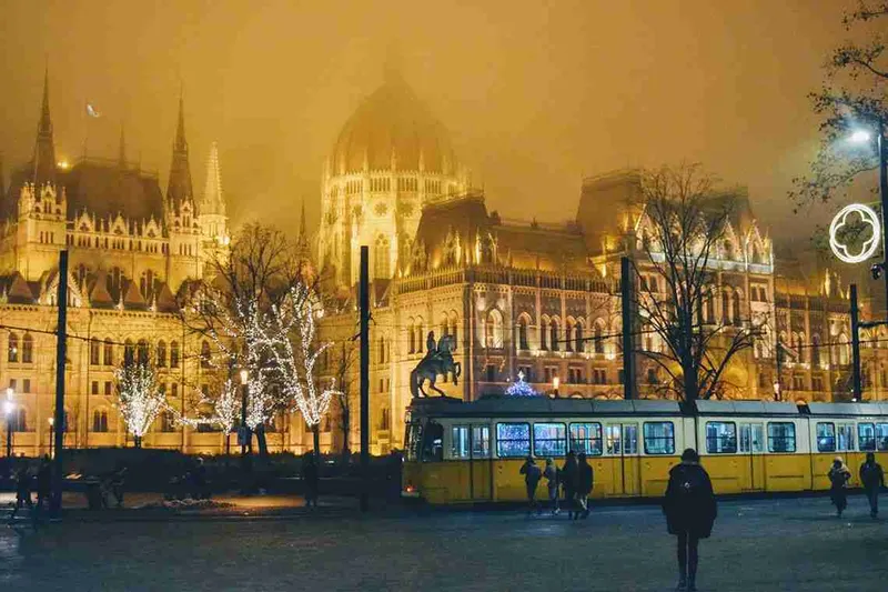 Tranvía amarillo pasando ante el Parlamento iluminado al atardecer