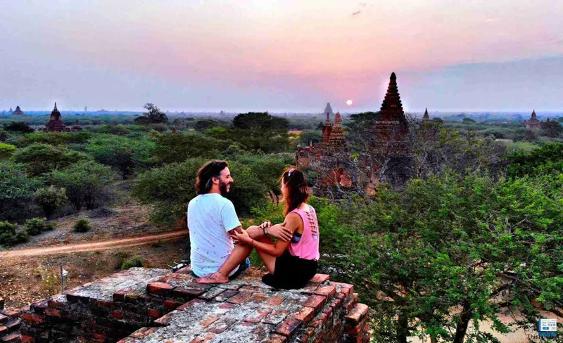 Pareja sentada en lo alto de un templo viendo la puesta de sol sobre Bagán