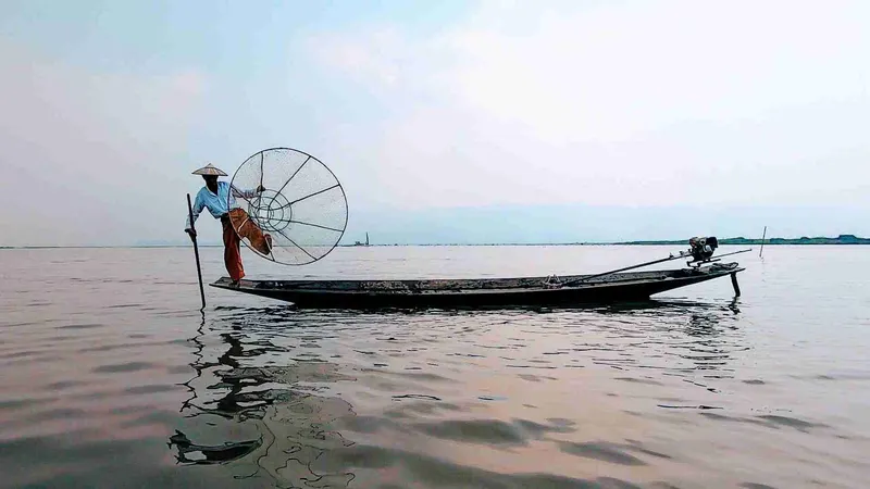 Pescador remando de pie con la nasa cónica en el lago Inle