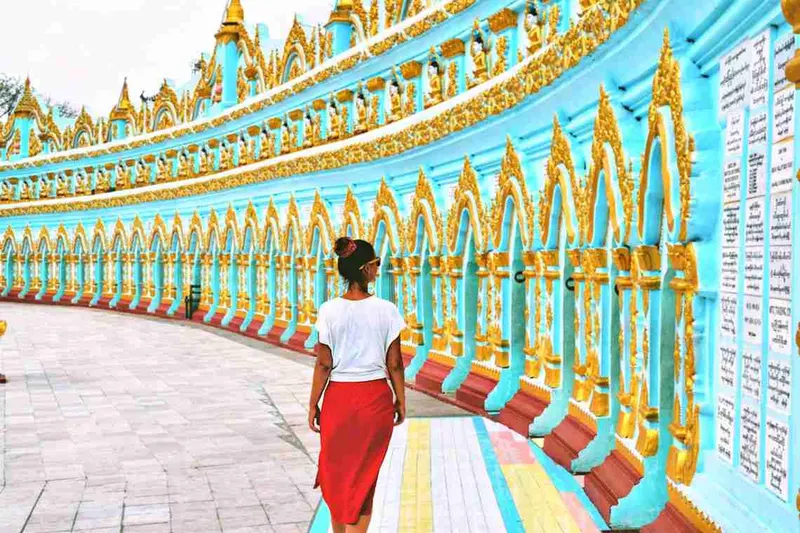 Mujer recorriendo la galería cubierta de un templo, con el techo dorado y turquesa