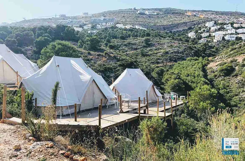 Tiendas de campaña del glamping repartidas por la ladera, unidas por una pasarela de madera