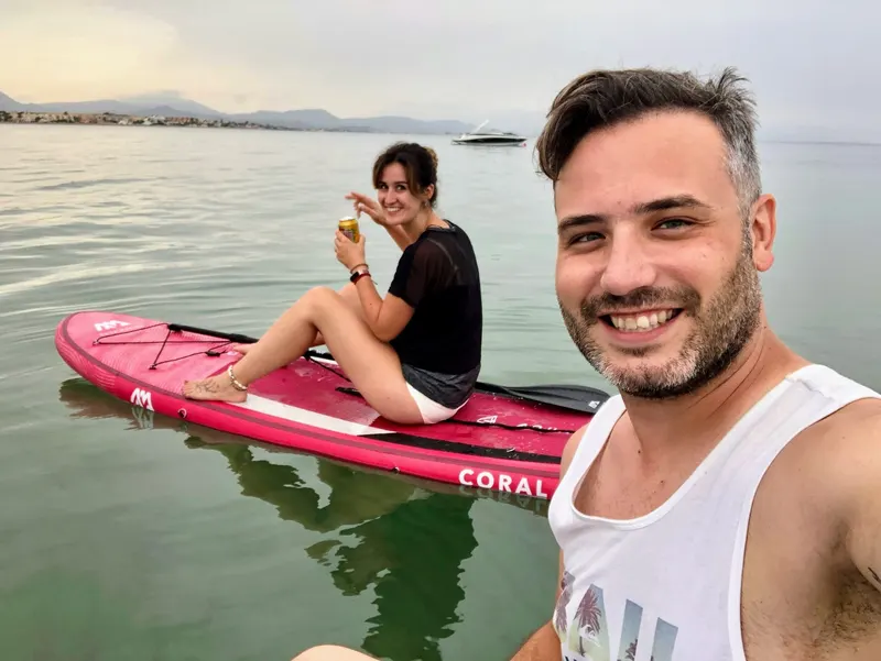 Pareja descansando sobre la tabla de paddle surf al atardecer, frente a la costa
