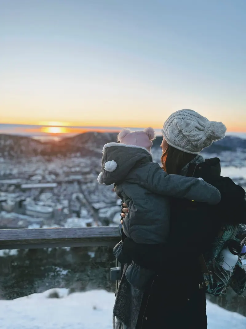 Madre con su hija en brazos viendo el atardecer sobre Bergen nevado desde el mirador