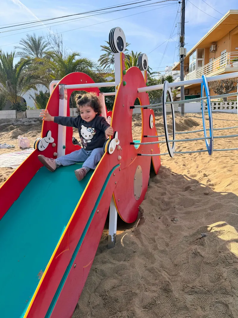 Niña tirándose por el tobogán del parque infantil de la playa de Dénia