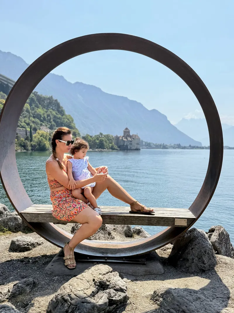 Madre e hija en un banco circular a orillas del lago Lemán, con el castillo de Chillon al fondo