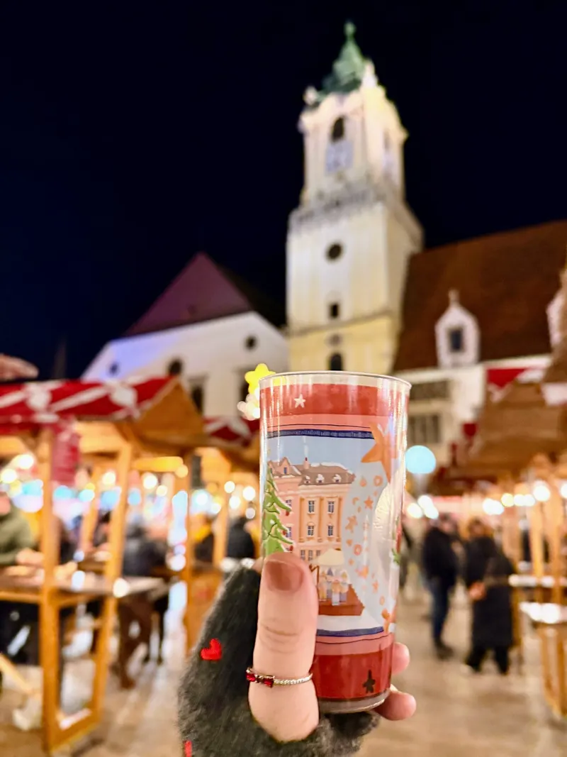 Vaso de vino caliente del mercado navideño con la torre del Antiguo Ayuntamiento al fondo