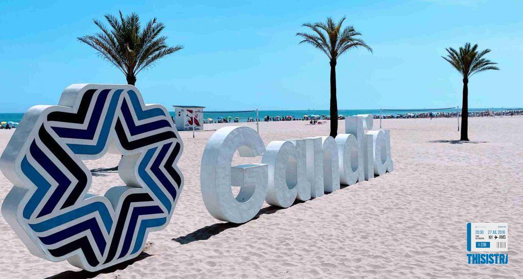 Letrero en la playa de Gandia y el fondo de palmeras y mar