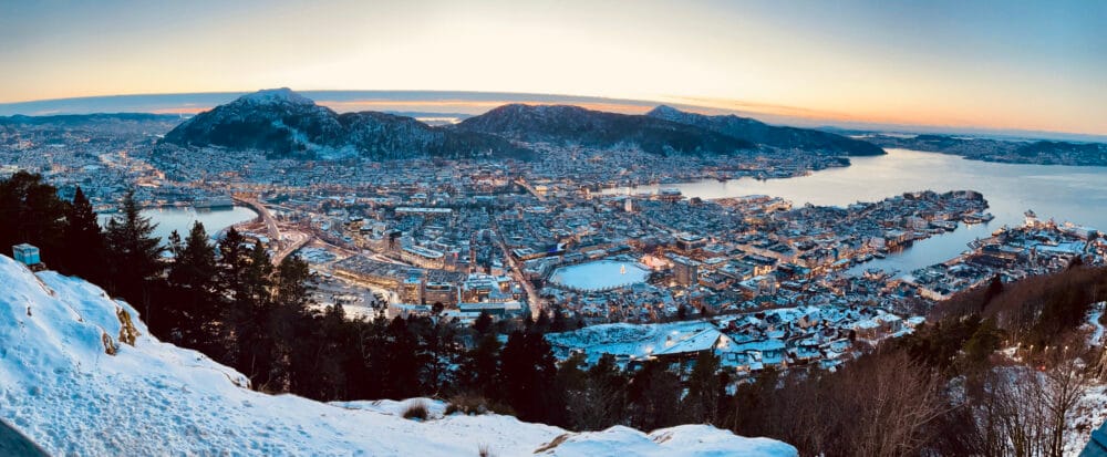 Puesta de sol de Bergen desde Monte Floyen con tonos violáceos y ciudad engalanada en navidad con nieve